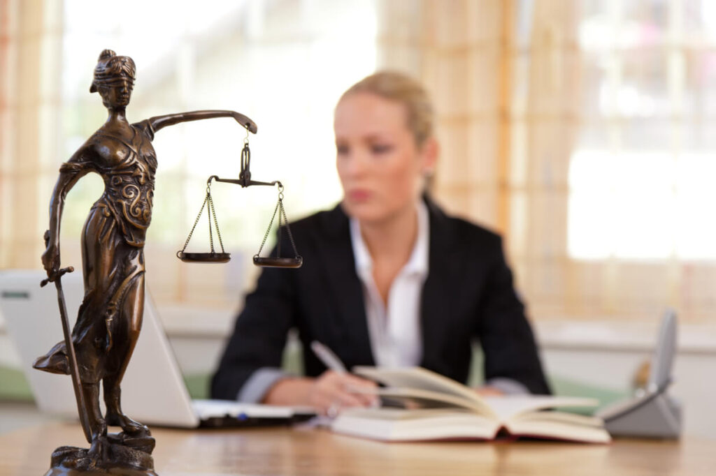 Lady Justice statue with lawyer working at desk background