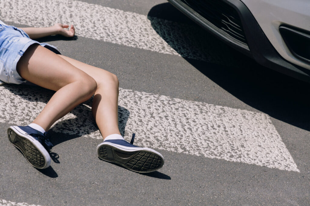 Child lying on pavement near parked vehicle