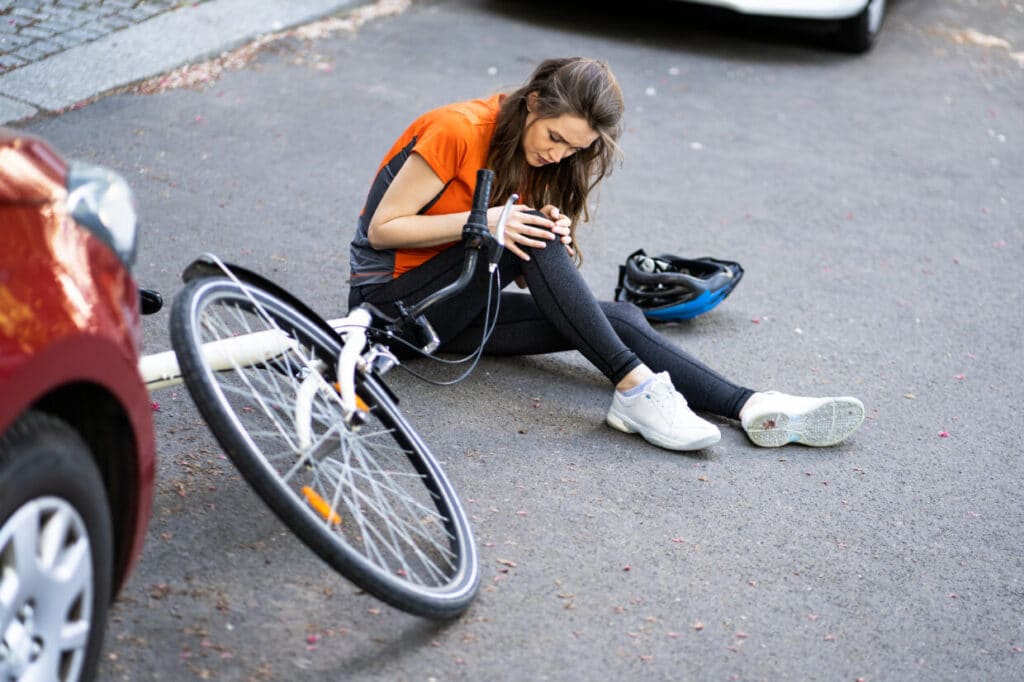 Woman cyclist sitting on road holding injured knee after accident