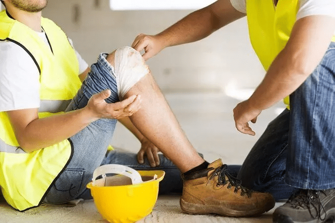 Construction worker receiving first aid bandage on leg injury