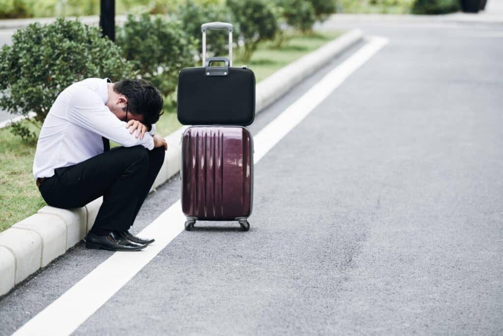 Distressed man crouching beside burgundy suitcase on road