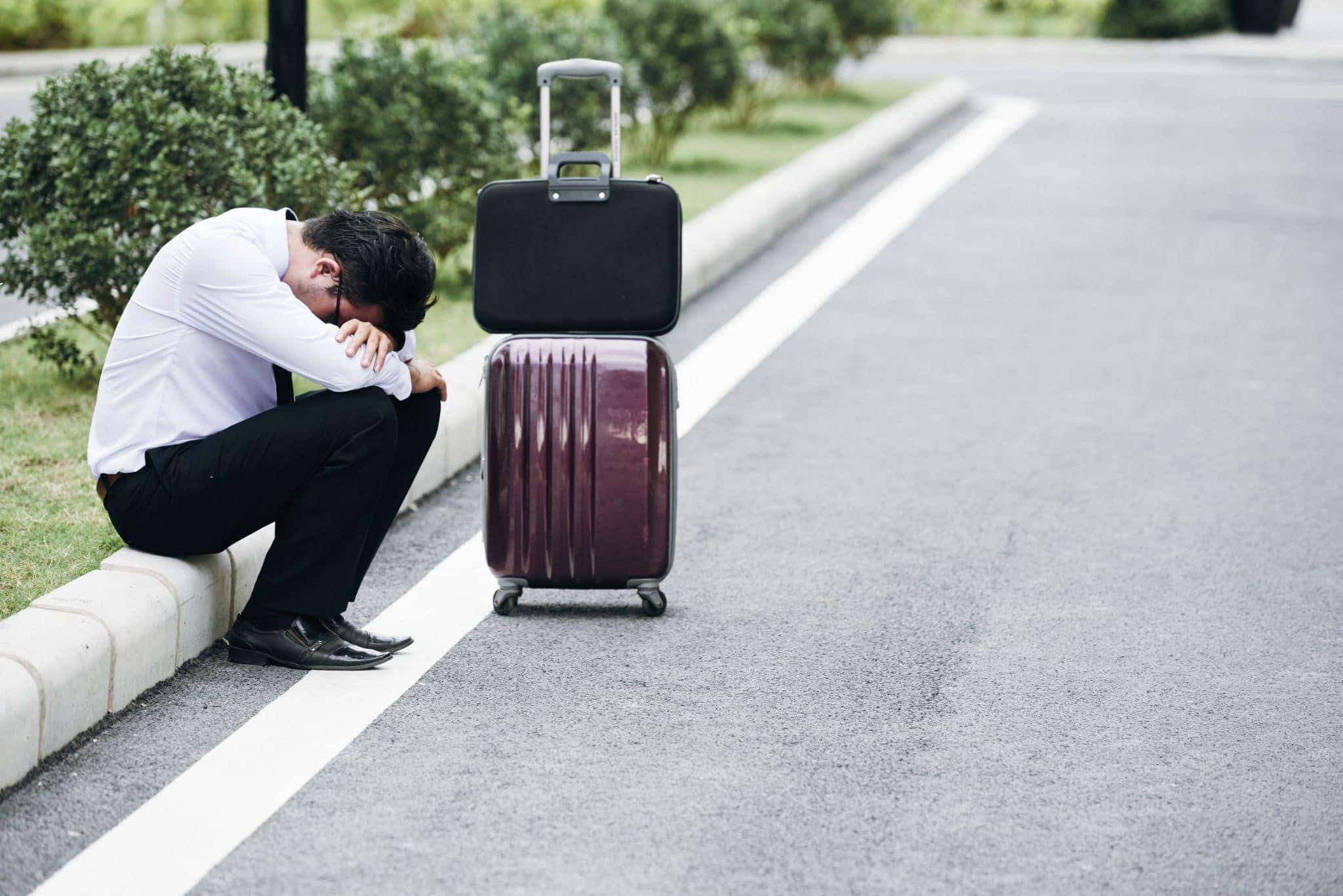 65479 Distressed man crouching beside burgundy suitcase on road